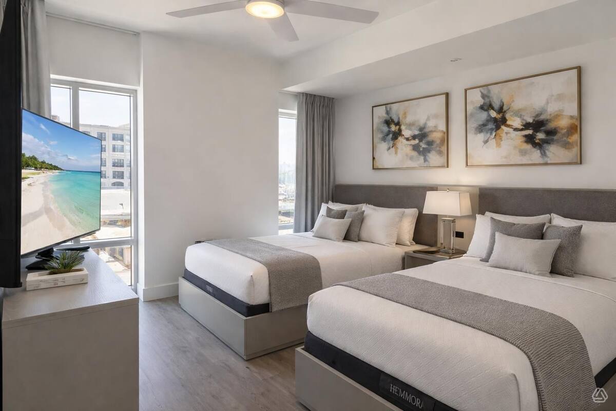 Habitación de hotel con dos camas, televisión, obras de arte y vista a la playa.