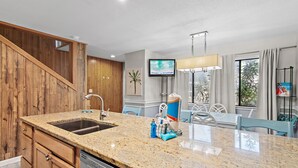A kitchen with granite countertops, wooden cabinets, a dishwasher, and a dining area with chairs and a table. - 🐚Gulf + Pool Views | Pet Friendly | Blue Surf 19🐚 (Miramar Beach)