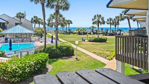 A pool area with a view of the beach, palm trees, and a white fence. - 🐚Gulf + Pool Views | Pet Friendly | Blue Surf 19🐚 (Miramar Beach)