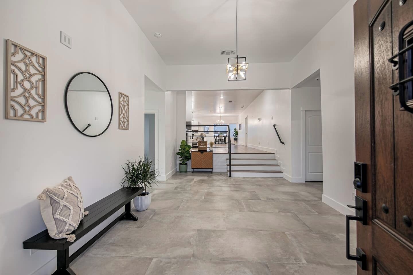 Un intérieur moderne avec un banc, une plante en pot, un miroir et un escalier menant à une autre pièce.