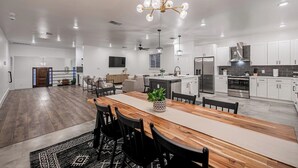Une cuisine moderne avec des meubles blancs, un réfrigérateur en acier inoxydable et un coin repas comprenant une table et des chaises en bois.