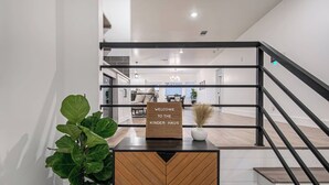 Un intérieur moderne avec un comptoir d’accueil en bois, une enseigne indiquant « BIENVENUE À LA KINDER HAUS », et un escalier avec des rampes noires.