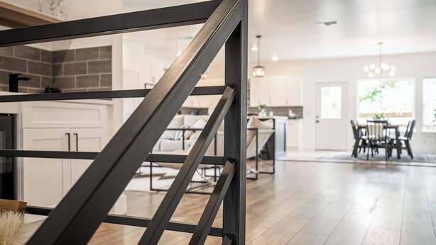 Une cuisine moderne avec un escalier en métal noir, un coin repas doté d’une table en bois et un espace de vie lumineux agrémenté d’un lustre.