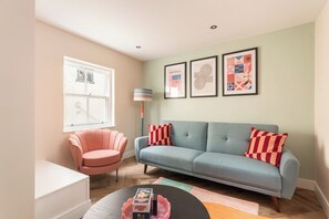 A living room with a sofa, a chair, a coffee table, and a lamp. There are framed pictures on the wall. - The Brighton Bliss - Sleeps 7 (Brighton)