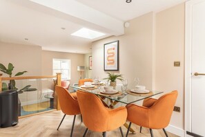 A dining area with a glass table, orange chairs, and a plant on the table. - The Brighton Bliss - Sleeps 7 (Brighton)