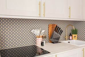 A kitchen with white cabinets, a patterned backsplash, and a countertop with kitchen utensils. - The Brighton Bliss - Sleeps 7 (Brighton)