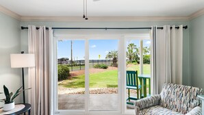 A room with a sliding glass door leading to a patio, a green chair, a patterned sofa, and a small table with a lamp and a plant. - 🏖️Steps to Beach | Pet Friendly | Pool | Ciboney 1001🏖️ (Miramar Beach)
