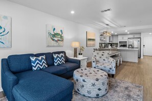 A modern living room with a blue sofa, ottoman, and matching chairs, a dining area with a bench, and a kitchen with white cabinets and appliances. - ☀️Pet Friendly | Steps to Beach | Pool | Ciboney 2014☀️ (Miramar Beach)
