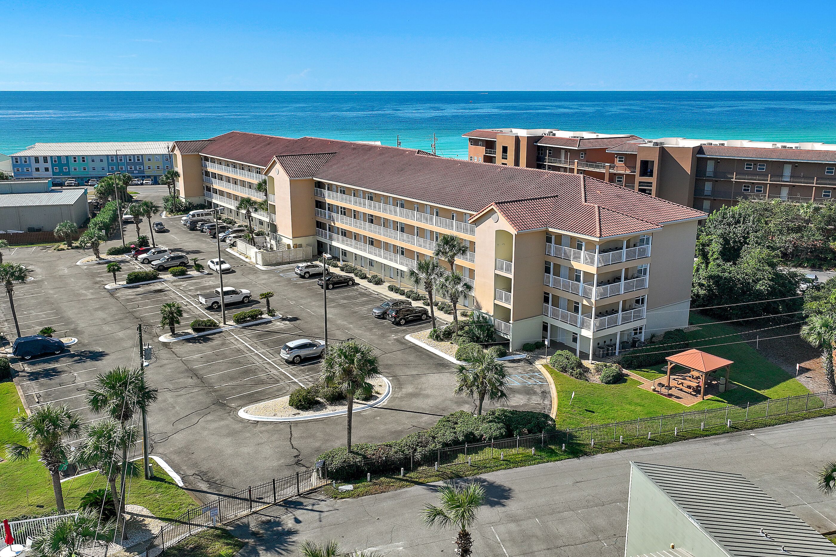 A multi-story hotel with a parking lot, a covered outdoor seating area, and a view of the ocean.