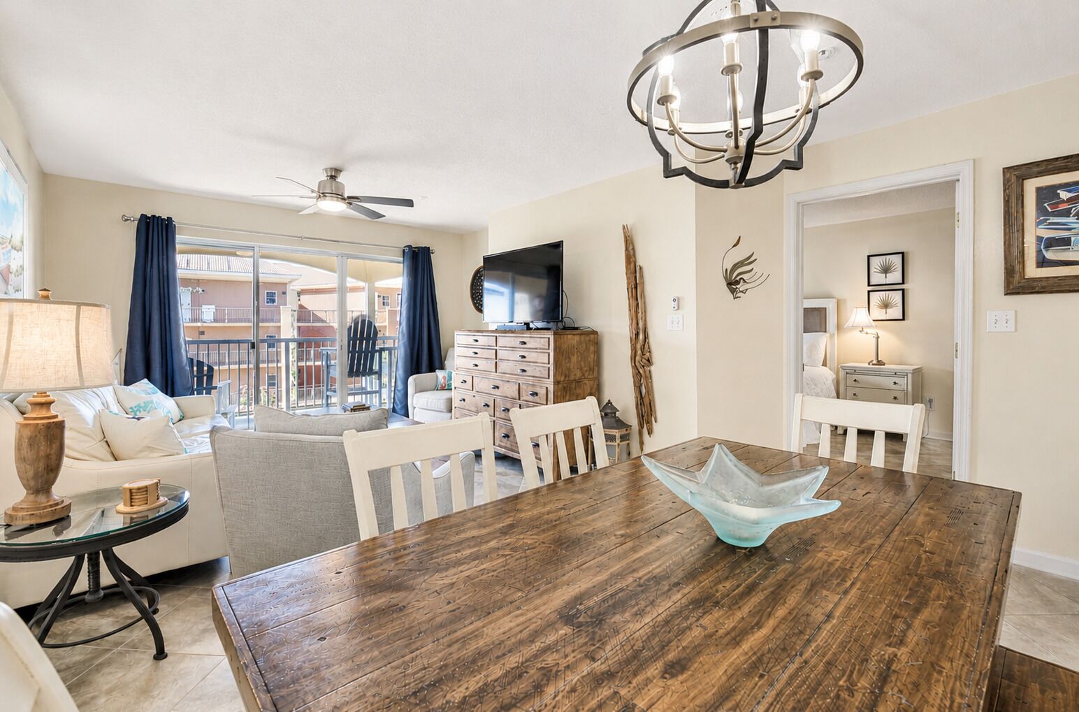 A dining area with a wooden table, chairs, a chandelier, and a view of the outside.