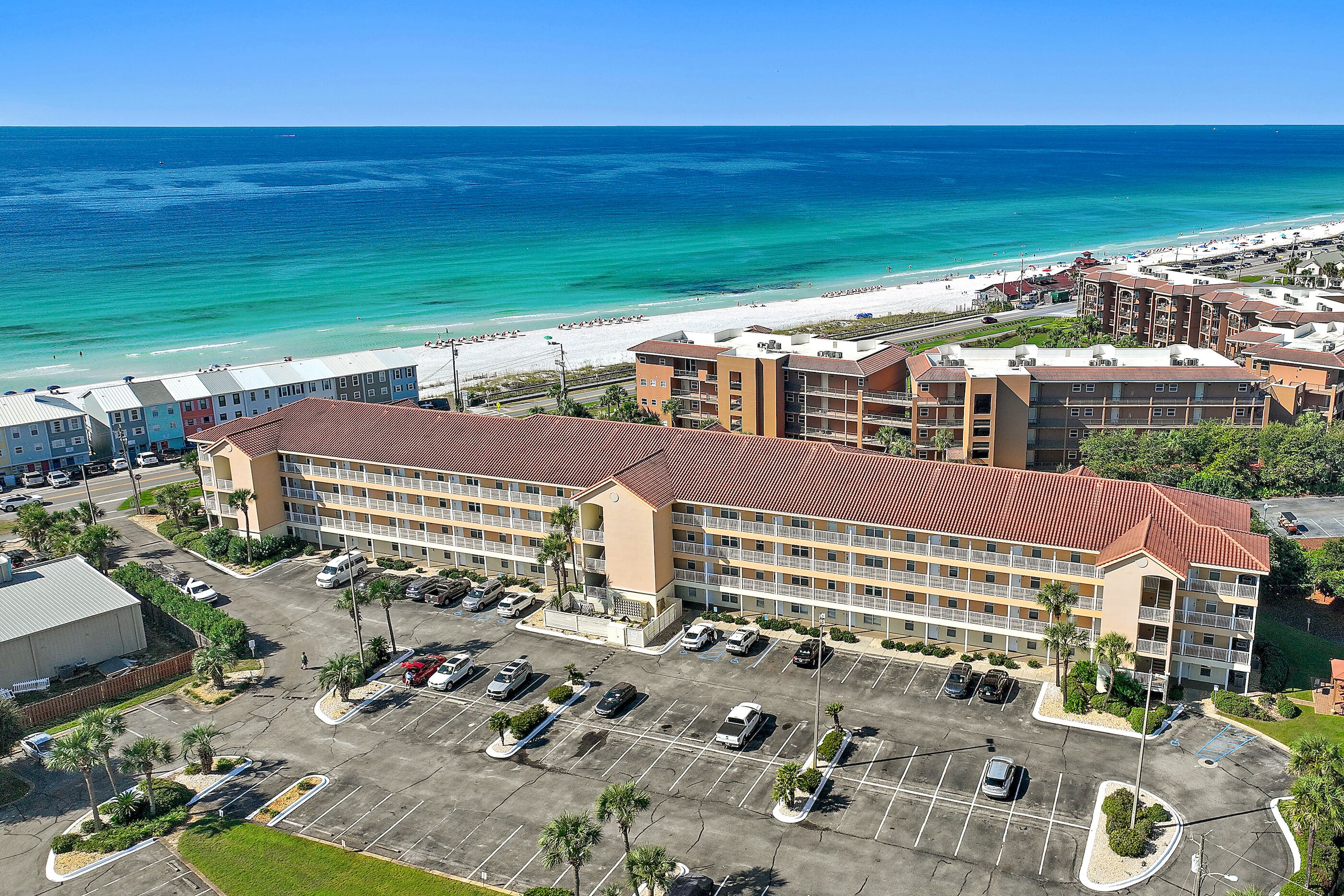 A hotel with multiple floors, a parking lot, and a beach view.