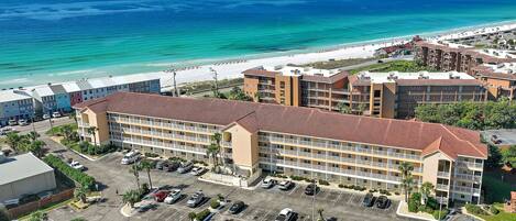 A hotel with multiple floors, a parking lot, and a beach view.