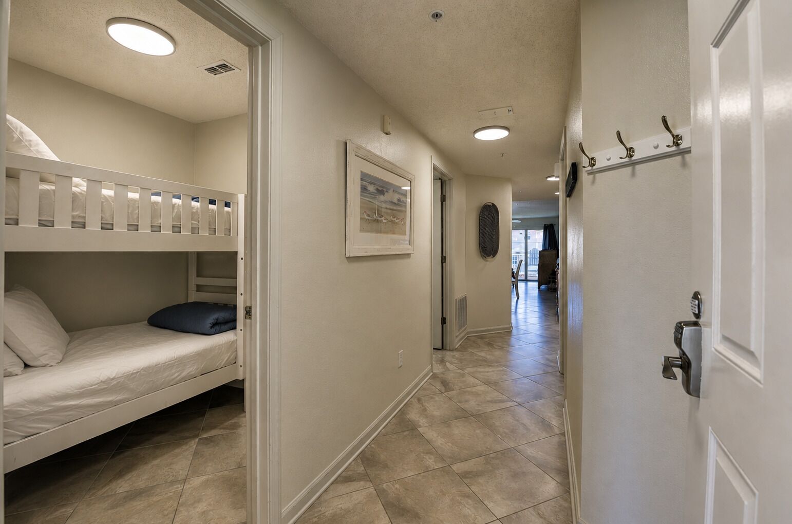 A hallway with bunk beds, a framed picture on the wall, and a door with a lock.