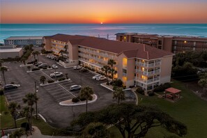 Ein Hotel mit mehreren Etagen, einem Parkplatz und Blick auf den Ozean bei Sonnenuntergang.