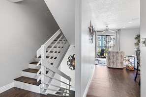 Eine Treppe mit weißen Geländern und dunklen Holzhäusern, ein Deckenventilator und ein Blick auf einen Balkon mit Gartenmöbeln.