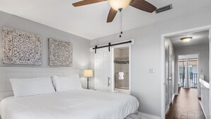 Een slaapkamer met een groot bed, een plafondventilator, een nachtkastje met een lamp en een inloopkast.