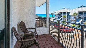 Een balkon met stoelen, uitzicht op het strand en een rij gebouwen met een blauw dak.