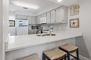 A kitchen with white cabinets, a white countertop, a sink, a microwave, and two stools.