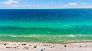 Ein Strand mit klarem türkisblauem Wasser, einem sandigen Ufer und einigen Sonnenschirmen.