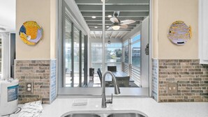 Eine Küche mit modernem Design, inklusive einer Spüle aus Edelstahl, einem Deckenventilator und Blick durch die Glastür auf die Terrasse.