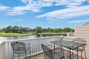Um terraço com mesa e cadeiras com vista para um lago e um campo de golfe ao fundo.