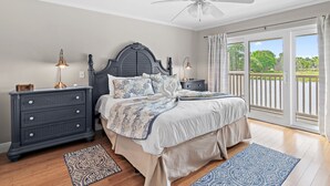 A bedroom with a bed, nightstands, a dresser, a ceiling fan, and a view through the window.