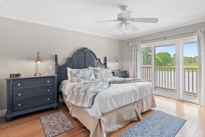 Ein Schlafzimmer mit Bett, Nachttischen, einem Schminktisch und einem Deckenventilator, mit Blick aus dem Fenster.