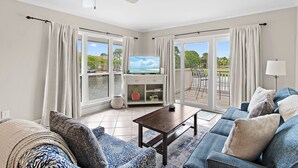 A living room with a TV, sofa, coffee table, and a view of the outdoors.