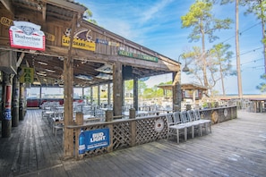 A wooden deck with tables and chairs, a sign for Bud Light, and a view of the ocean. - 🏖️Golf Cart(LSV) | Pet Friendly | SanDestin Resort | Sugar Sands🏖️ (Miramar Beach)