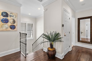 A hallway with a wooden floor, a staircase with a black railing, a large mirror, and a potted plant. - 🏖️Golf Cart(LSV) | Pet Friendly | SanDestin Resort | Sugar Sands🏖️ (Miramar Beach)