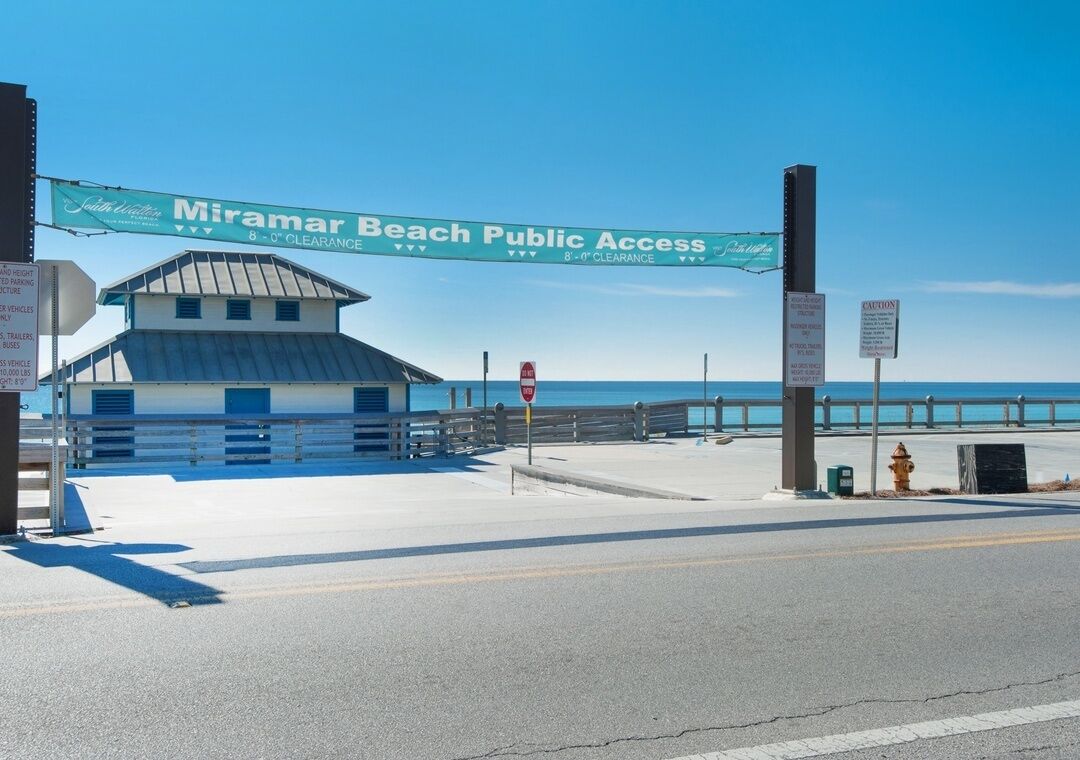 A beach access sign, a building, a stop sign, a fire hydrant, and a clear sky.