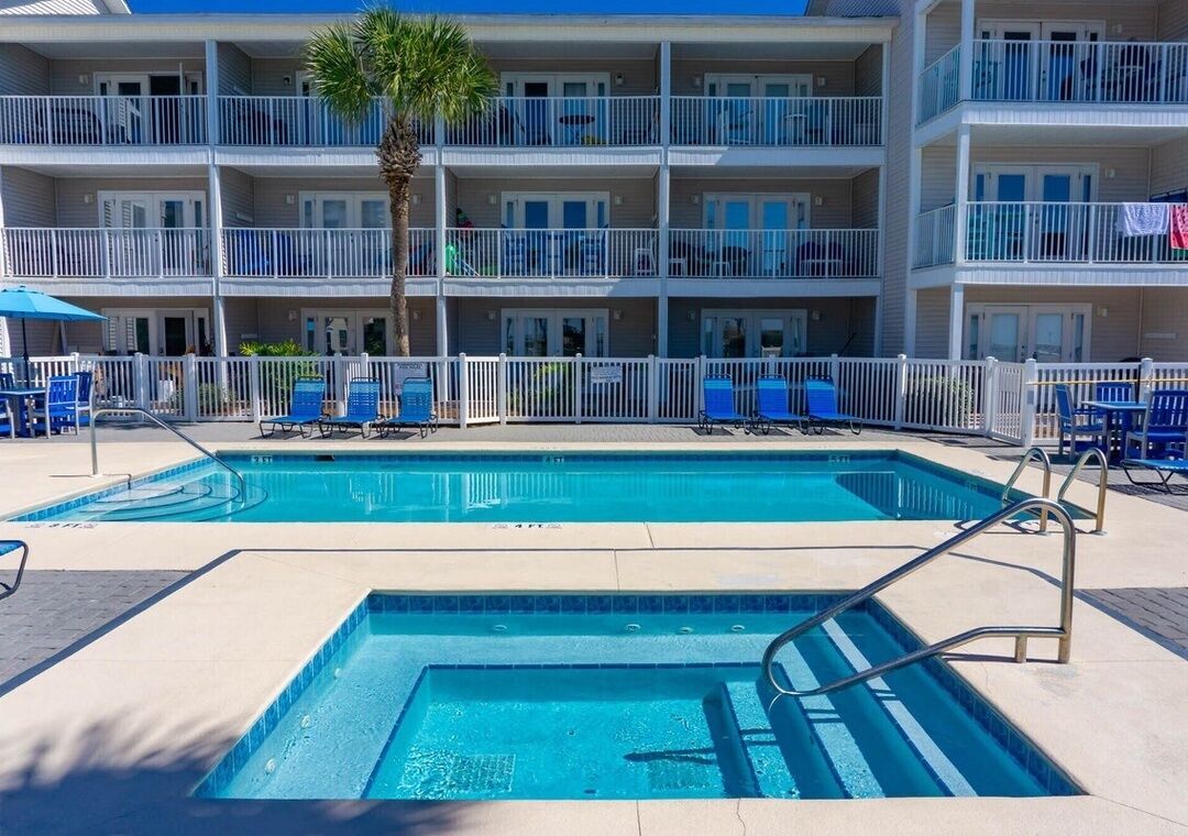 A hotel with a swimming pool, multiple balconies, and lounge chairs.