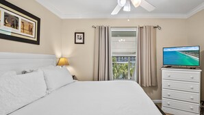 Hotelkamer met een bed, een televisie, een plafondventilator, een raam met gordijnen en een ingelijst beeld aan de muur.