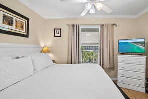 A hotel room with a bed, a TV, a ceiling fan, a window with curtains, and a framed picture on the wall. - 🌴Summerspell 305 | Gulf Views | Pool + Hot Tub🌴 (Miramar Beach)