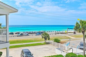 Blick auf einen Strand mit blauem Himmel, einen Parkplatz mit mehreren Autos und eine Fahne an einem Mast.