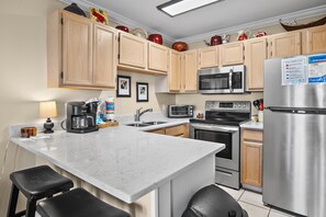 A modern kitchen with wooden cabinets, stainless steel appliances, a marble countertop, and bar stools. - 🌴Summerspell 305 | Gulf Views | Pool + Hot Tub🌴 (Miramar Beach)