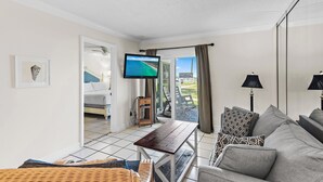 Ein Wohnzimmer mit einer Couch, einem Tisch, einem Fernseher und einem Balkon mit Blick.