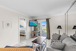 Ein Wohnzimmer mit einer Couch, einem Tisch, einem Fernseher und einem Balkon mit Blick.