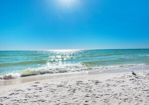 Ein Strand mit blauem Himmel, ruhiger See und Fußspuren im Sand.
