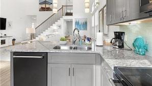 Una cocina moderna con una isla central, electrodomésticos de acero inoxidable y una escalera que lleva a un nivel superior.