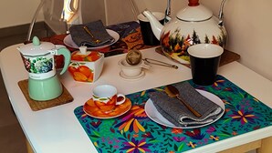 A table with a teapot, cups, a strainer, and a floral placemat. - Thumbelina House (Sapri)