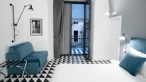 A room with a bed, a blue sofa, a black and white checkered floor, a door leading to a balcony, and a framed picture on the wall. - Suite Pulcinella (Naples)