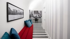 A hallway with a black and white striped floor, a red bench with blue cushions, and a framed cityscape picture on the wall. - Suite Pulcinella (Naples)