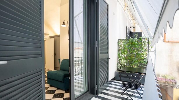 A narrow corridor with a checkered floor, a sliding glass door leading to a balcony, and a green plant on the right. - Suite Pulcinella (Naples)