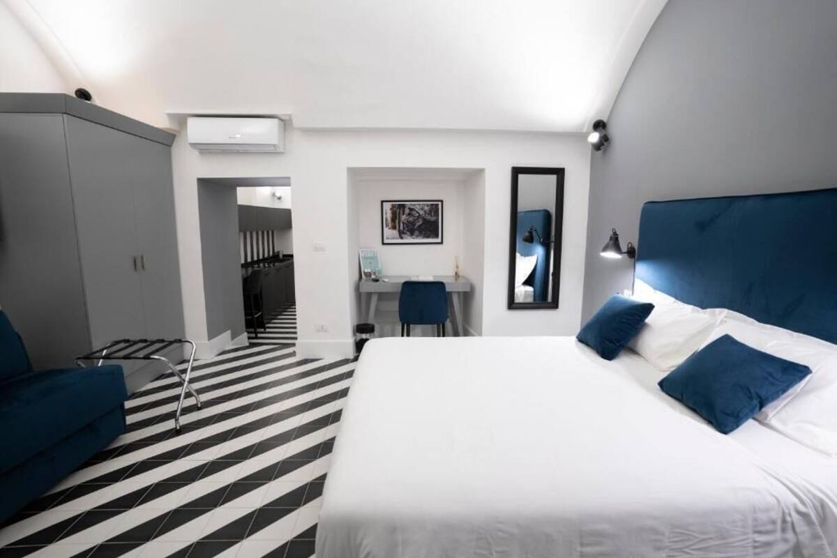 A hotel room with a bed, a desk, a chair, a wardrobe, and a mirror.