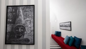 A modern interior with a striped wall, a framed abstract artwork, a red sofa with blue cushions, and a black and white patterned floor. - Suite Pulcinella (Naples)