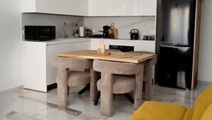 Una cucina moderna con mobili bianchi, un frigorifero nero, un tavolo di legno con due sedie e un divano giallo.