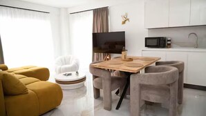 Un soggiorno moderno con un divano, un tavolino rotondo, una televisione e un angolo cottura con pensili e un forno a microonde.