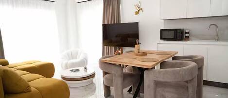 A modern living room with a sofa, a round coffee table, a TV, and a kitchen area with cabinets and a microwave.