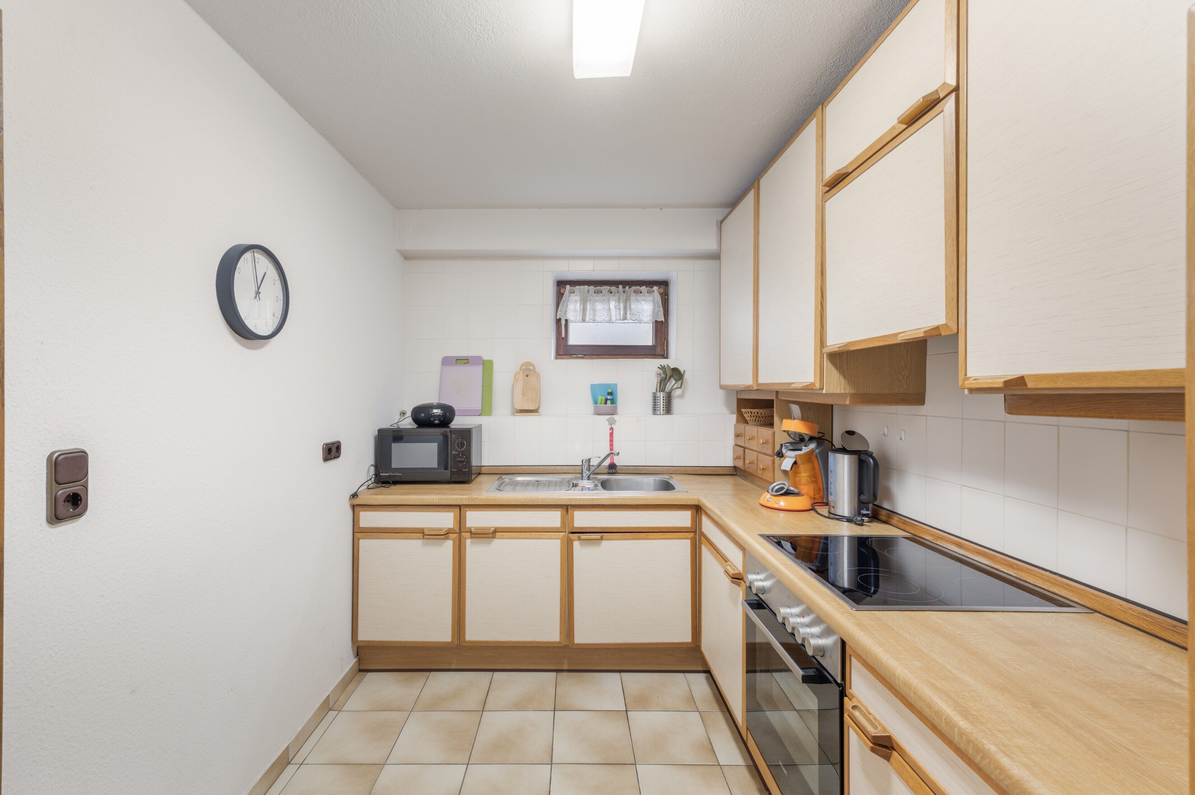 Cocina compacta con microondas, tostadora, hervidor y un reloj en la pared.